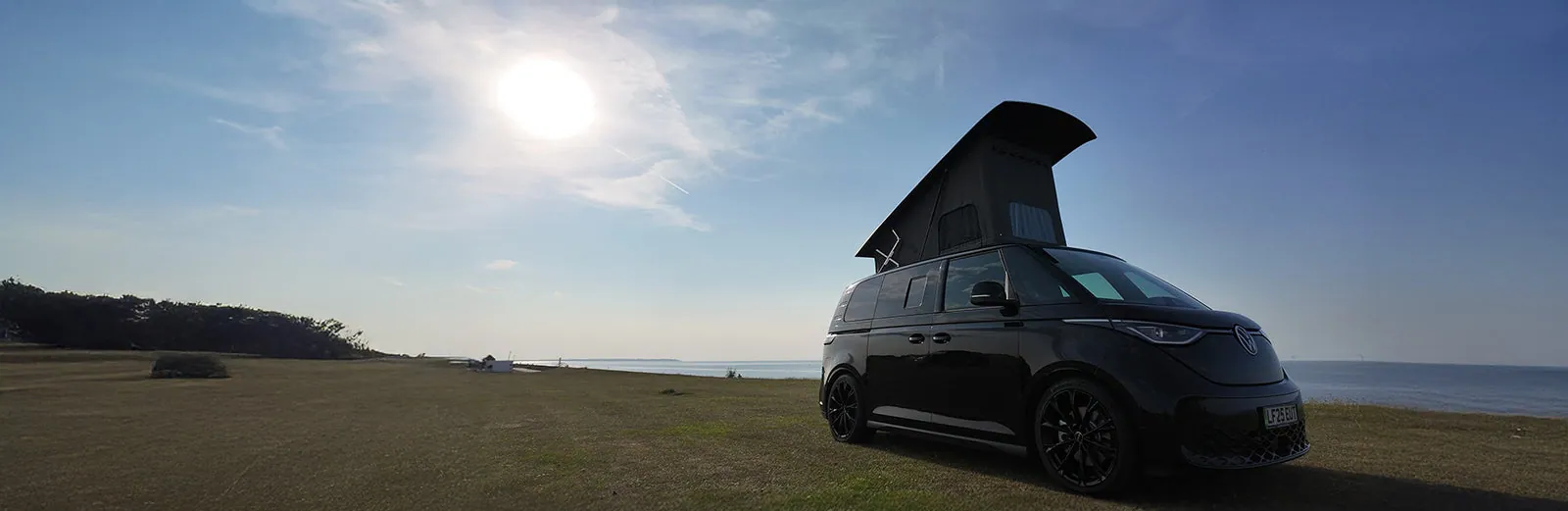 VW ID. Buzz camper with pop-top roof on the coast at sunset
